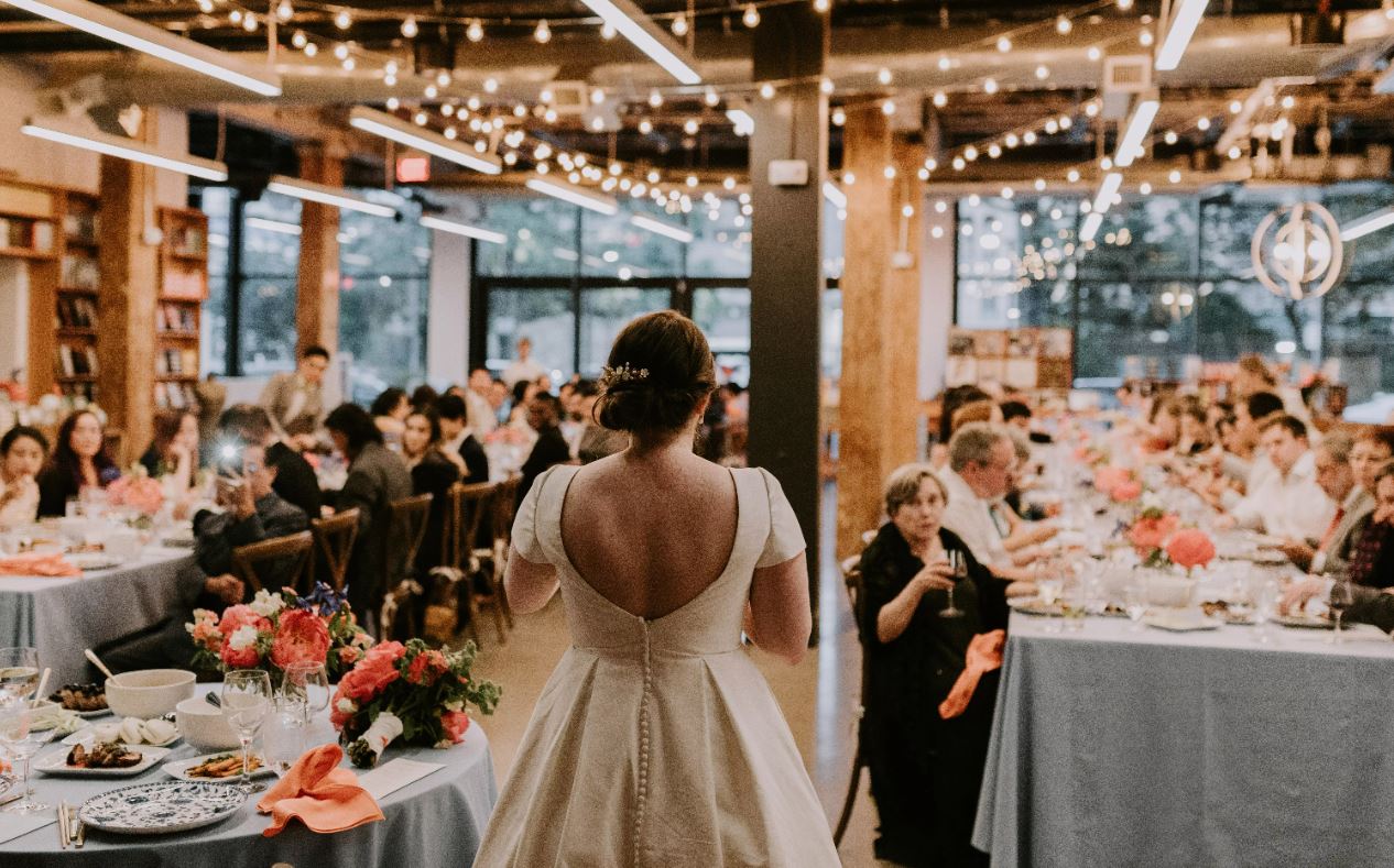 Guests and flowers surround a wedding reception area, framing a bride standing gracefully in her white gown