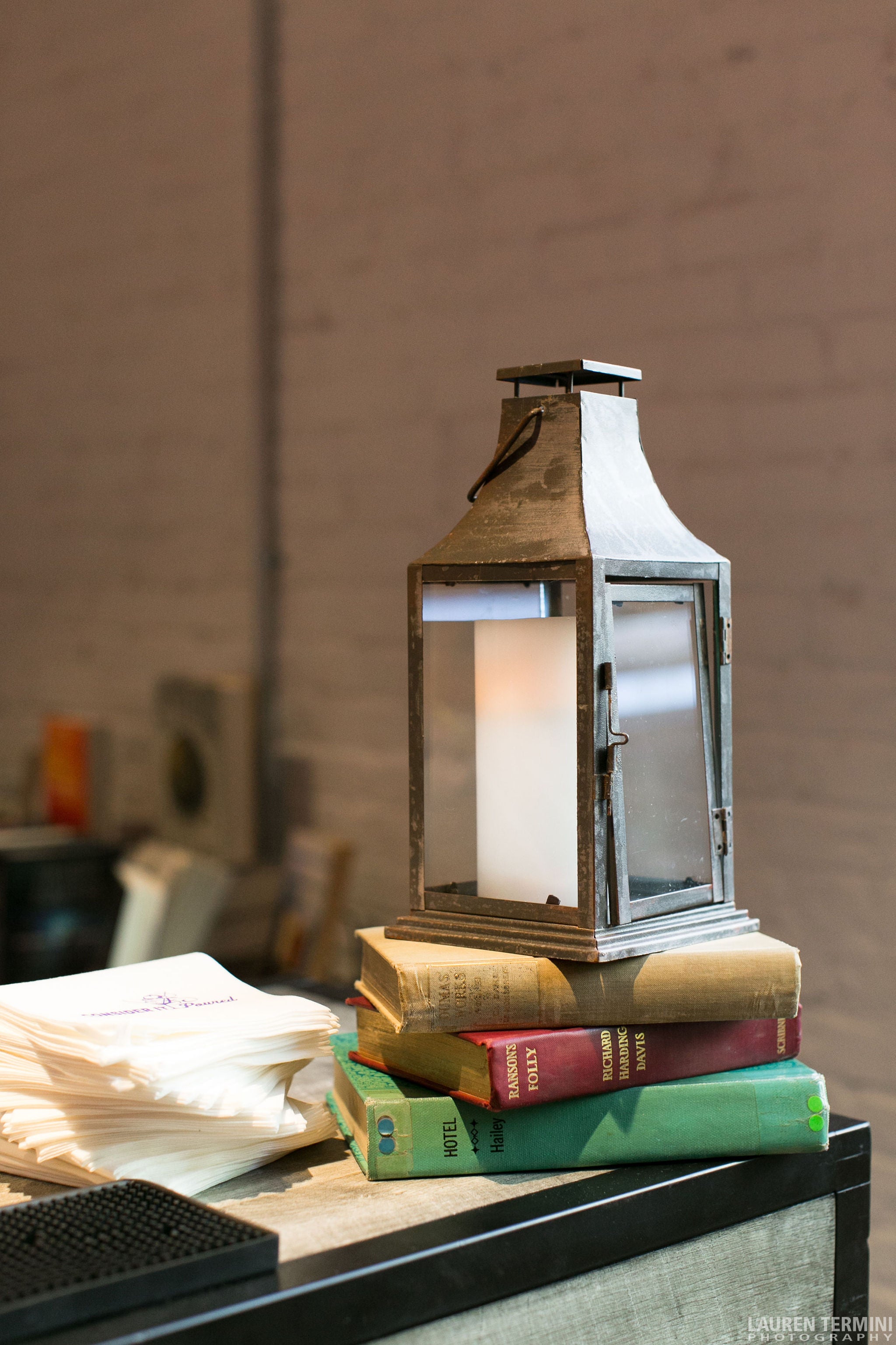 Pile of books of different colors stacked on top of each other with a lamp on top and napkins beside