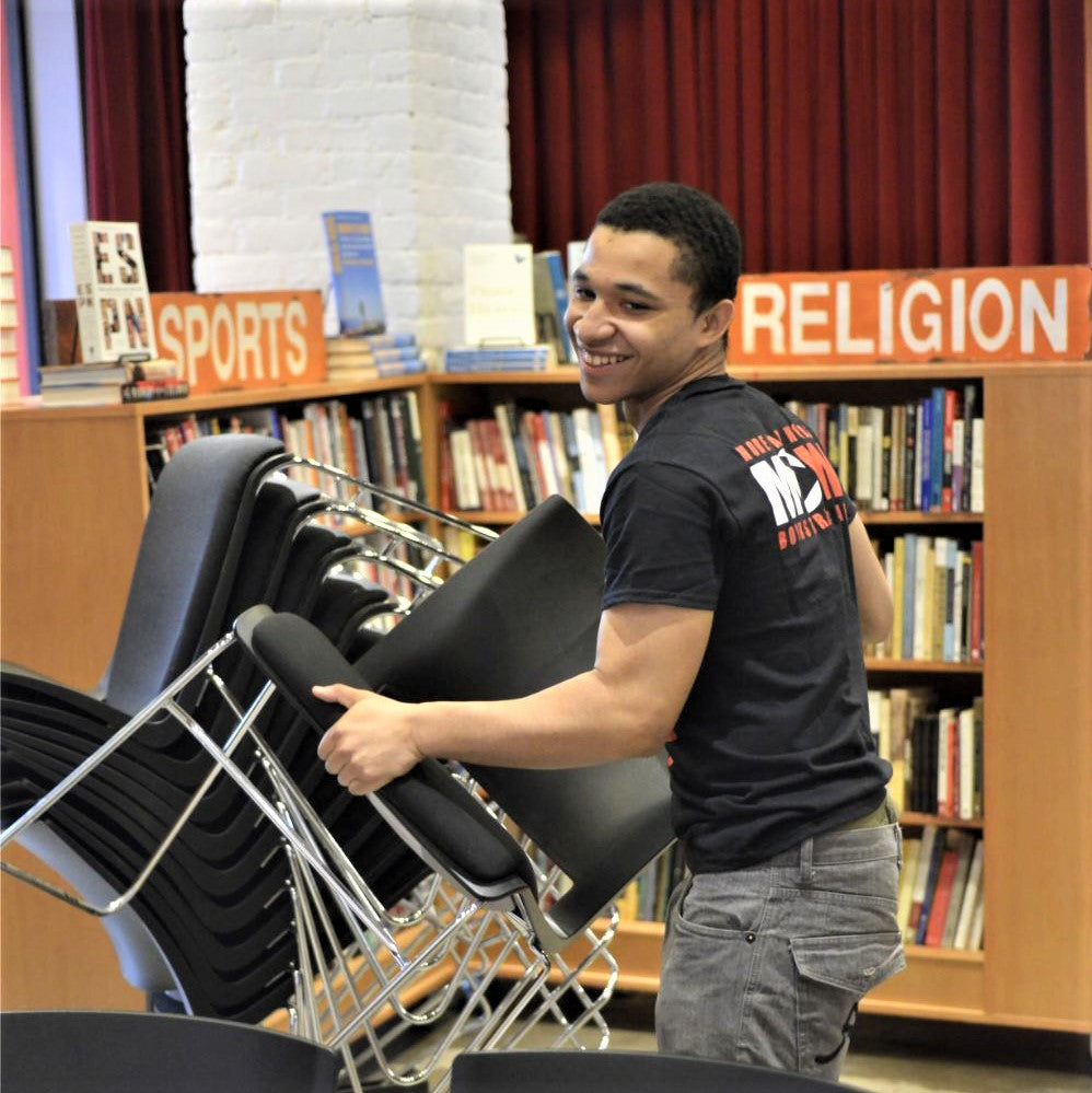 One of More Than Words' Youth is rearranging chairs in a library, possibly for an event or to tidy up the space