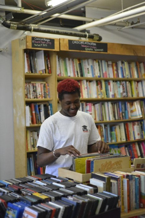 A youth from More than Words, engrossed in browsing a well-stocked bookstore, amid neatly arranged shelves filled with books