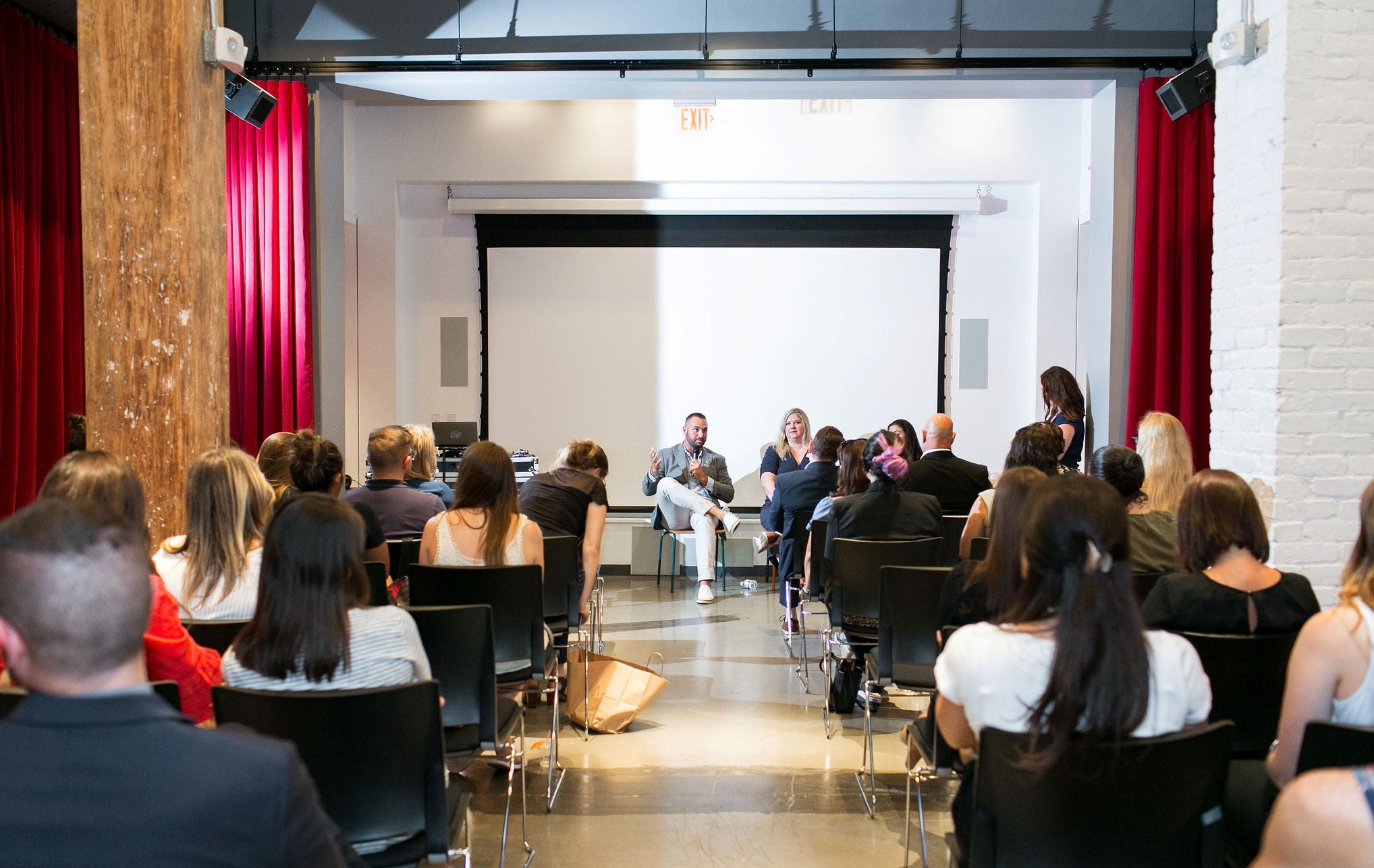 A gathering of individuals seated in chairs within a room, engaged in conversation and possibly attending a meeting or event