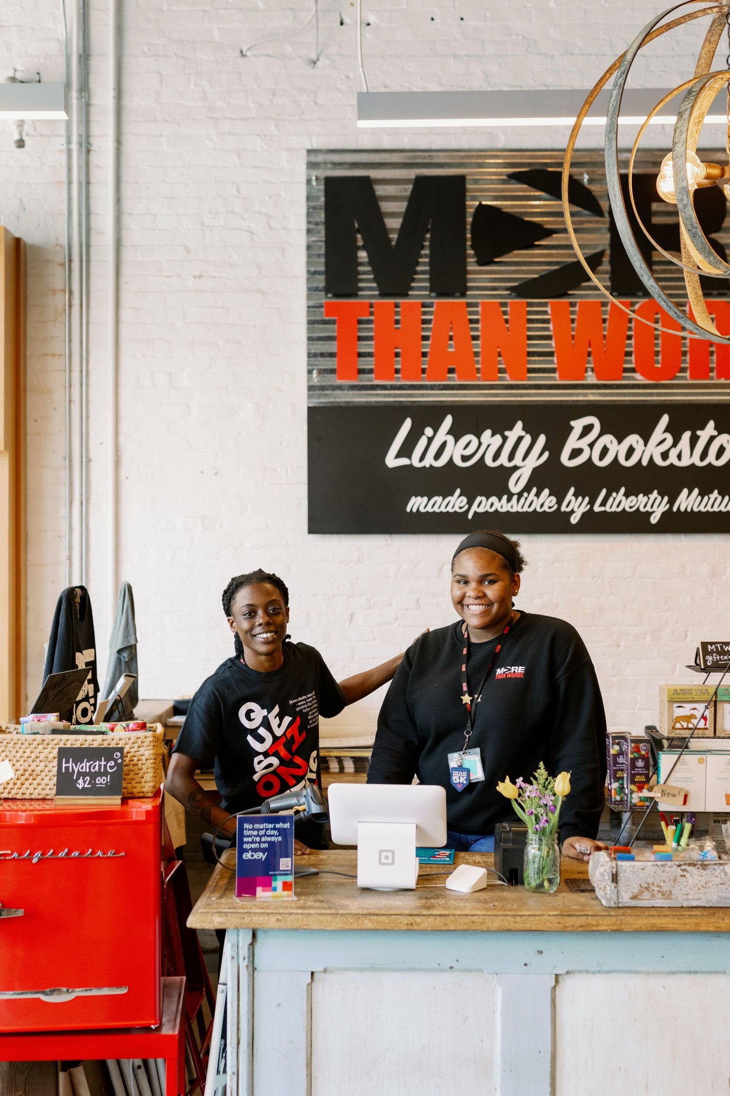 Two women wearing professional attire stand behind a bookstore counter, surrounded by neatly arranged shelves of books