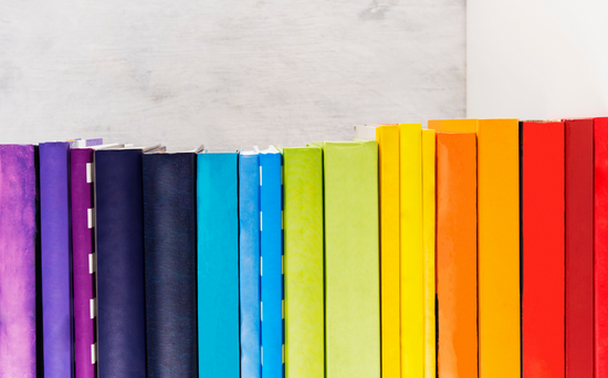 Books displaying the colors of the rainbow rest gracefully upon a pristine white shelf