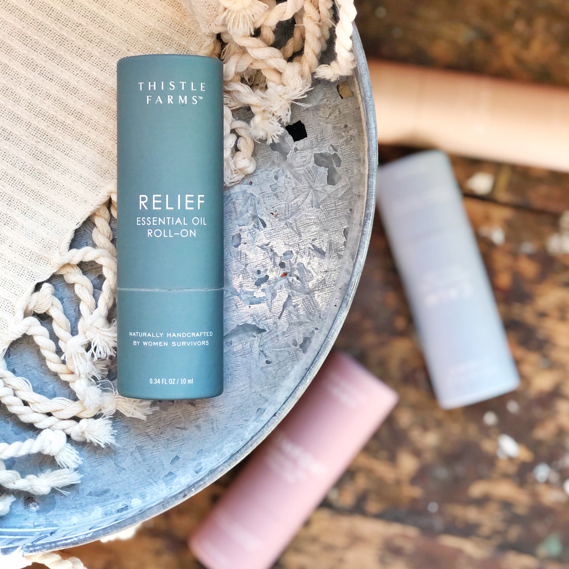 A teal container of Thistle Farms relief essential oil roll on a metal tray