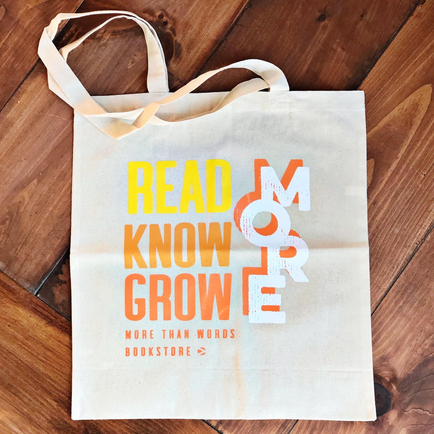 A tote bag displaying the phrase "Read Know Grow" in bold white, yellow, and orange letters against a rustic wooden backdrop