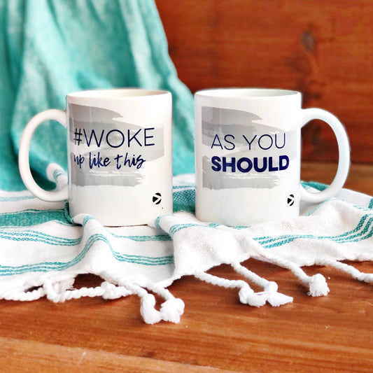 Two white More Than Words' mugs on white cloth with hashtags #AsYouShould and #WokeUpLikeThis, on a red wooden backdrop